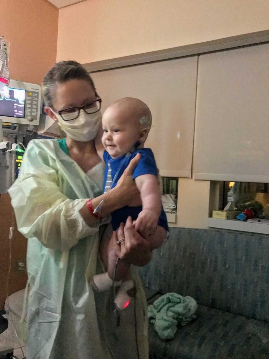 Mother stands in hospital room wearing mask while holding son with acute lymphoblastic leukemia