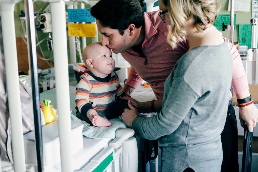 Father leans over to kiss son in hospital crib who has acute lymphoblastic leukemia