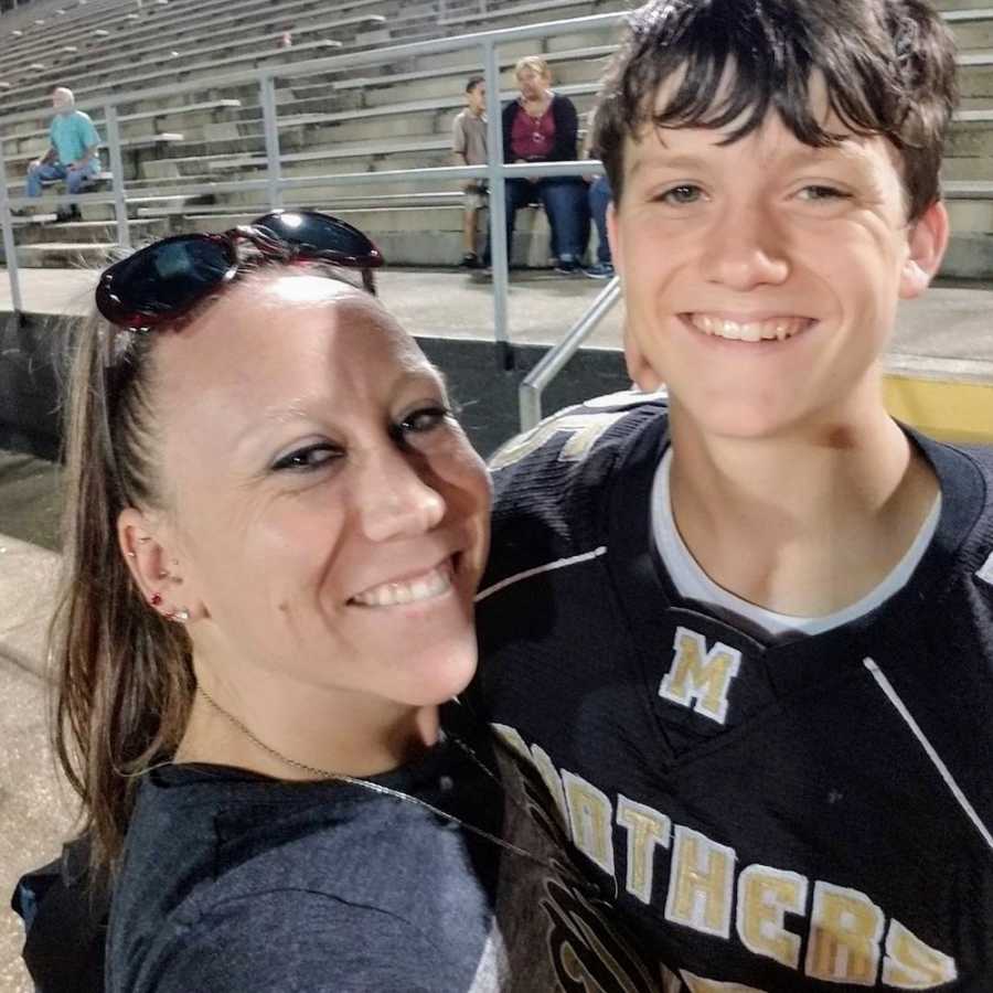 Mother smiles in selfie with teen son in football uniform