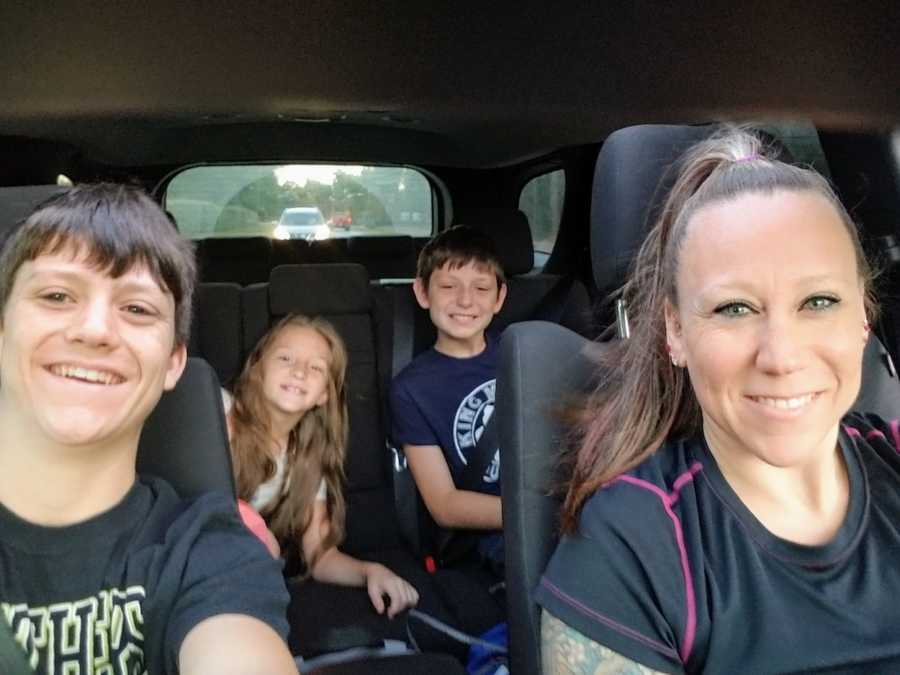 Teen boy takes selfie in car with his mom and two younger sibling in back seat