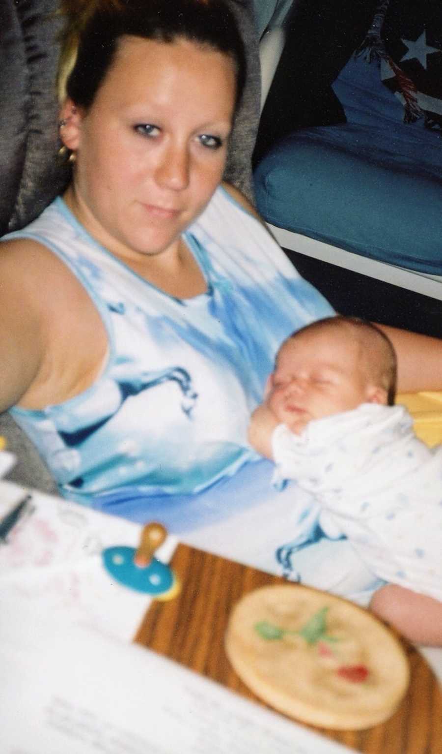 Woman sits in chair with baby asleep in her lap