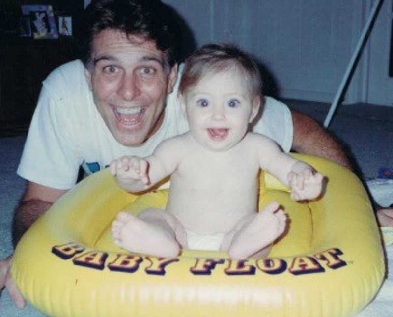 Father smiles beside baby daughter who sits on yellow float that says, "baby float"
