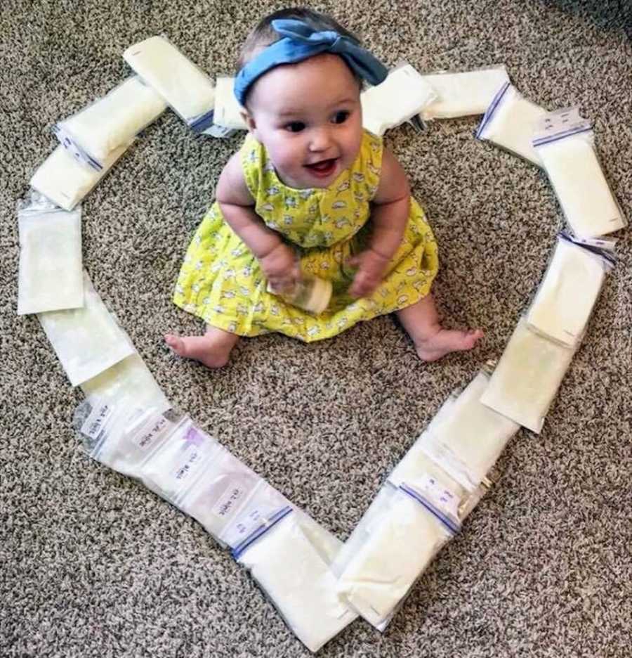 Baby girl sits on floor of home with donated milk shaped in heart around her