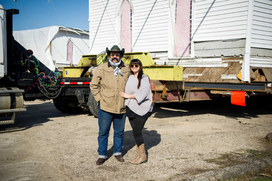 Husband and wife stand in front of moving truck that is moving parts of church that they saved