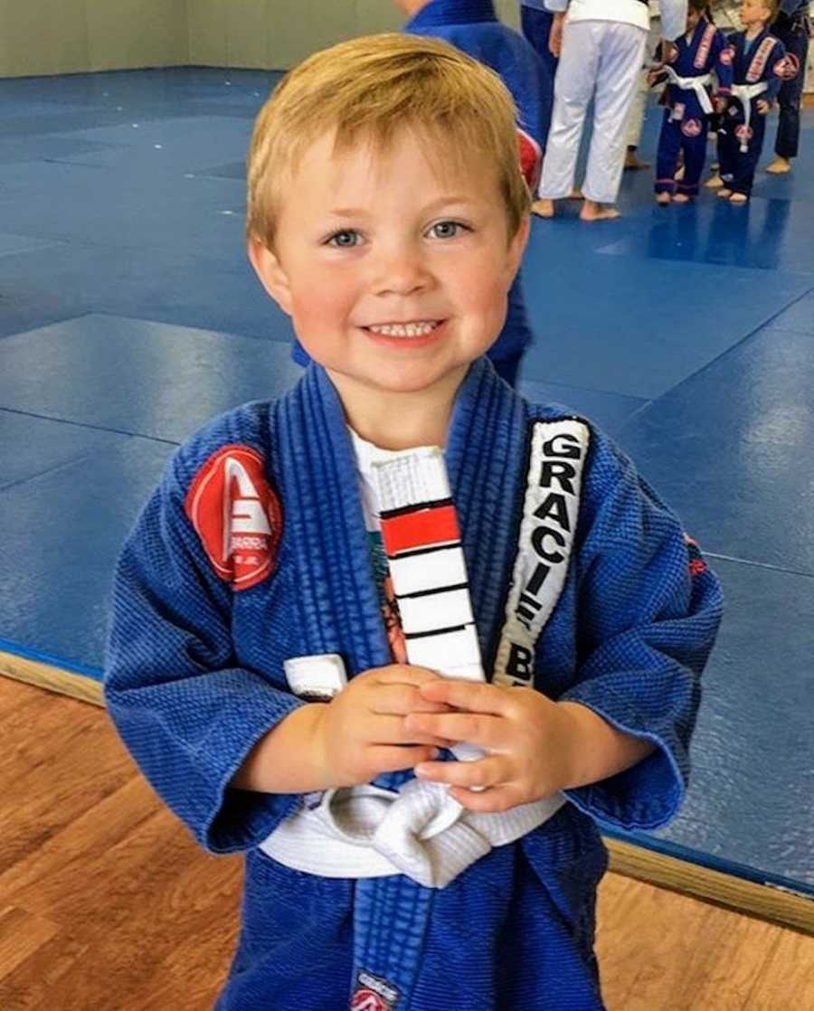 Little boy smiling as he stands in blue karate outfit