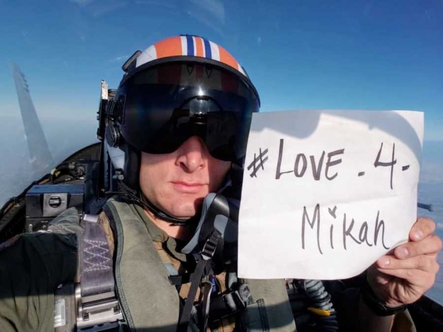 Fighter pilot sitting in plane holding up piece of paper that says, "Love 4 Micah"