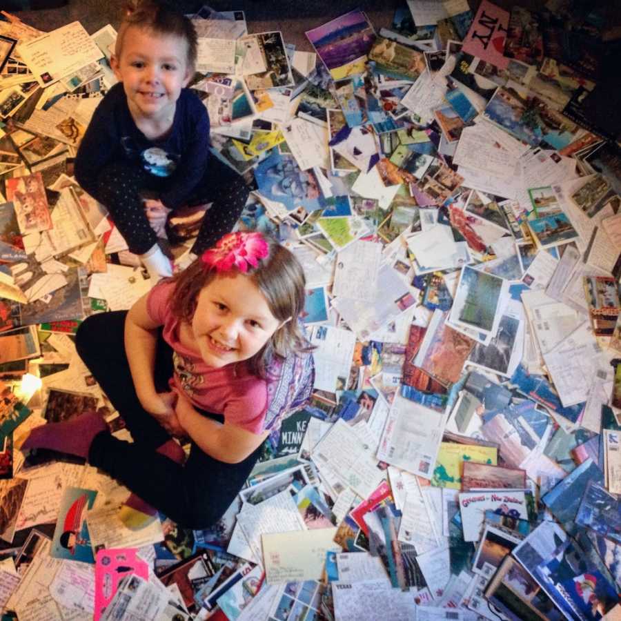 Little girl who went through chemo sits on floor covered in postcards with another little girl