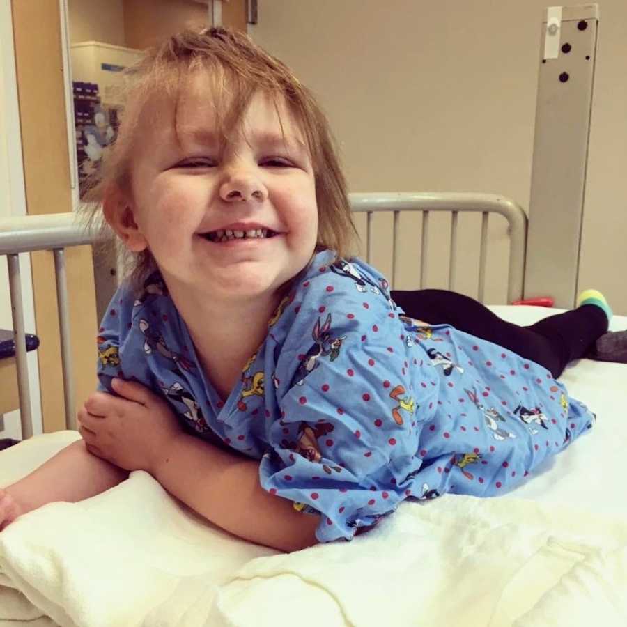 Little girl who has since passed lays on stomach in hospital bed smiling