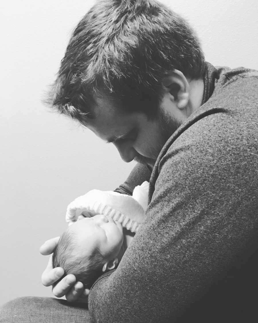 Father looks down as he holds newborn in his arms