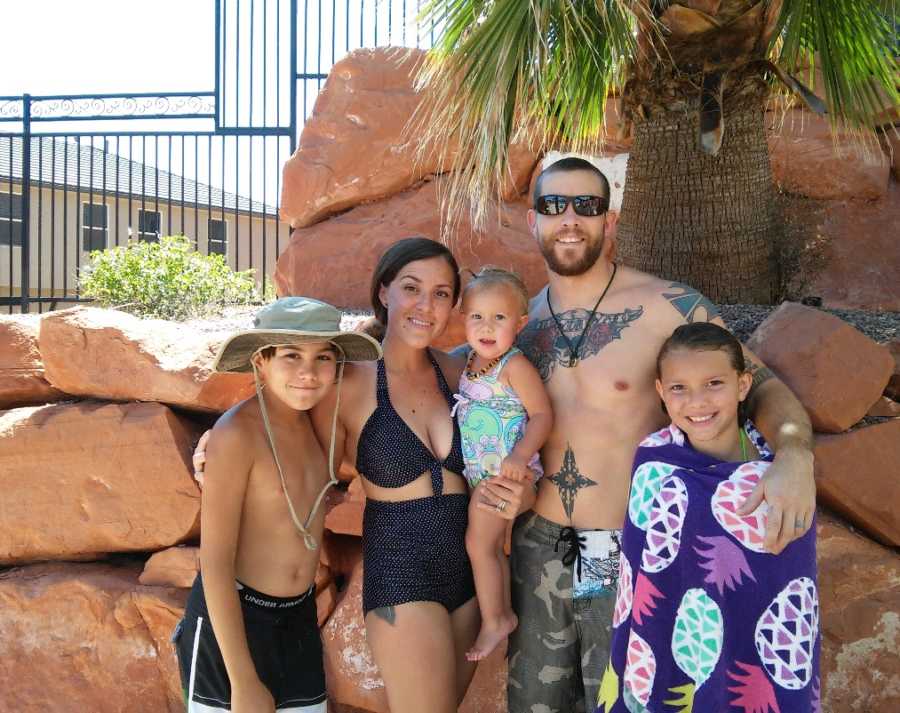 Husband and wife stands outside in bathing suits with their three children