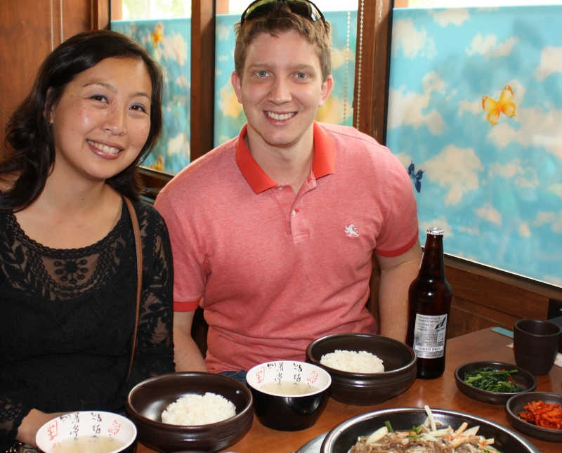 Korean woman sits at restaurant table full of Korean food beside husband