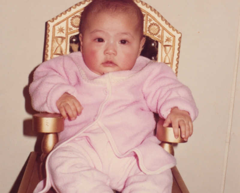 Baby sits in chair wearing light pink outfit