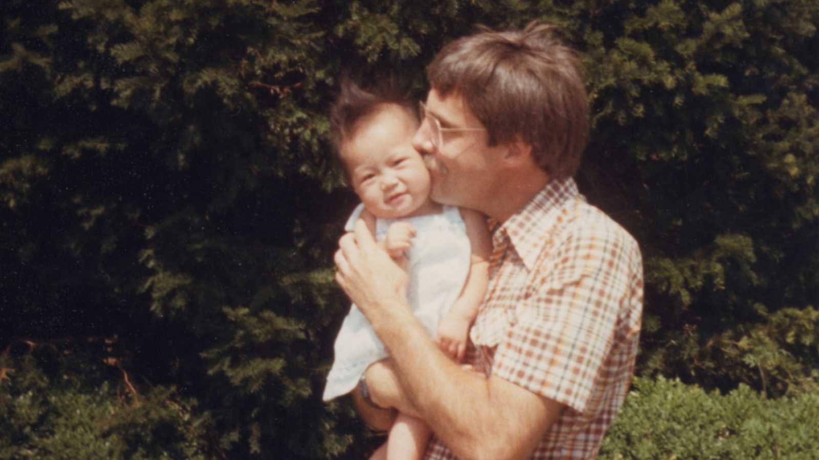 Father stands outside holding and kissing cheek of adopted daughter