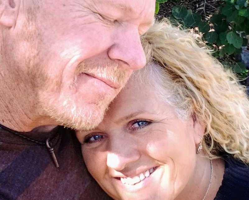 Wife smiles in selfie as she hugs husband with cancer