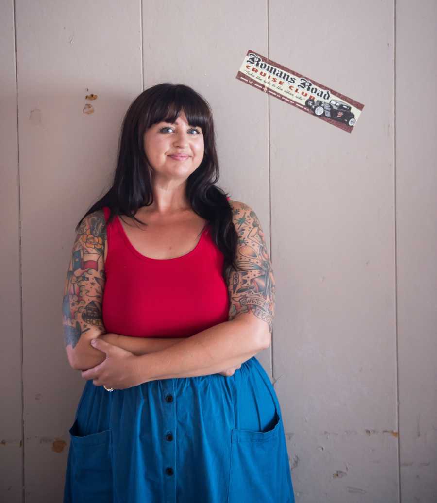 Woman stands smiling beside bumper sticker on wall that reminds her of her late father