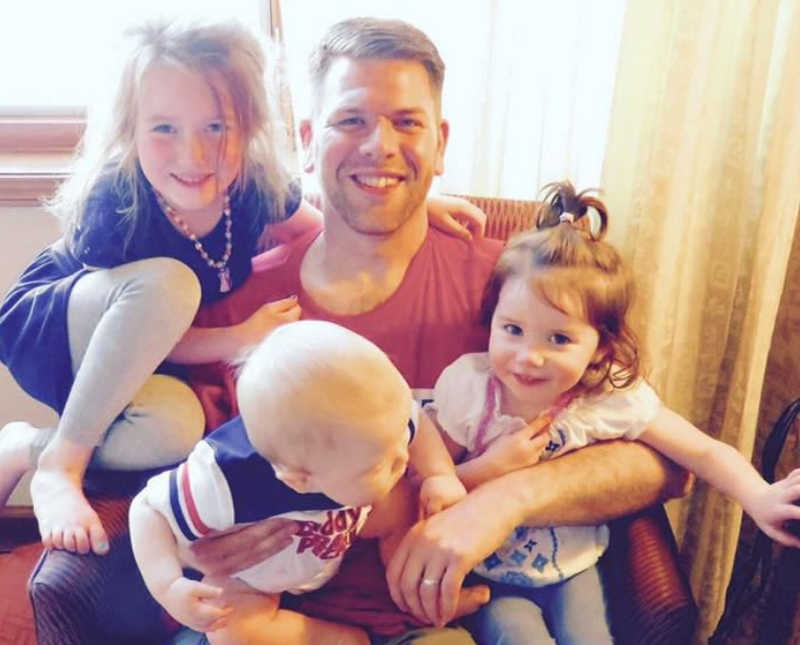 Father sits in chair with three children in his lap