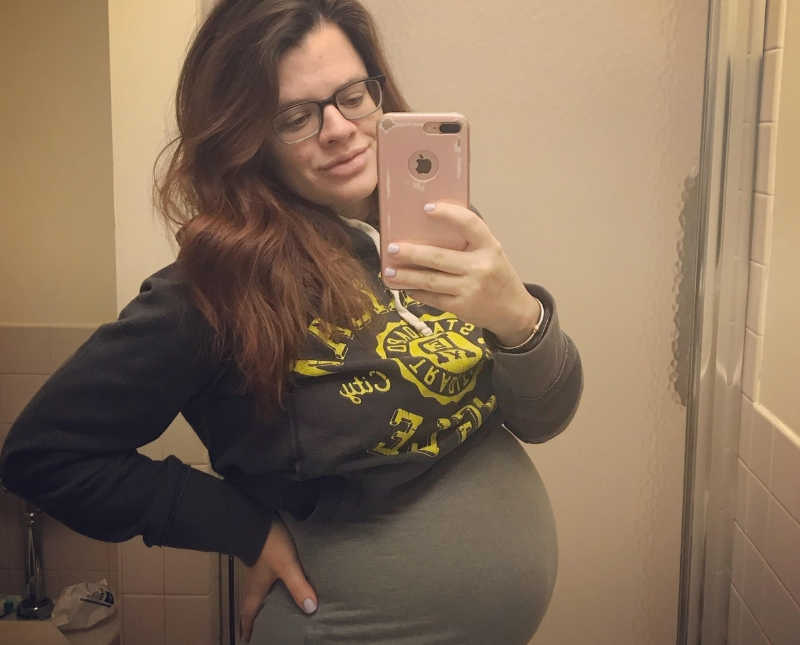 Pregnant woman smiles in mirror selfie with hand on her hip