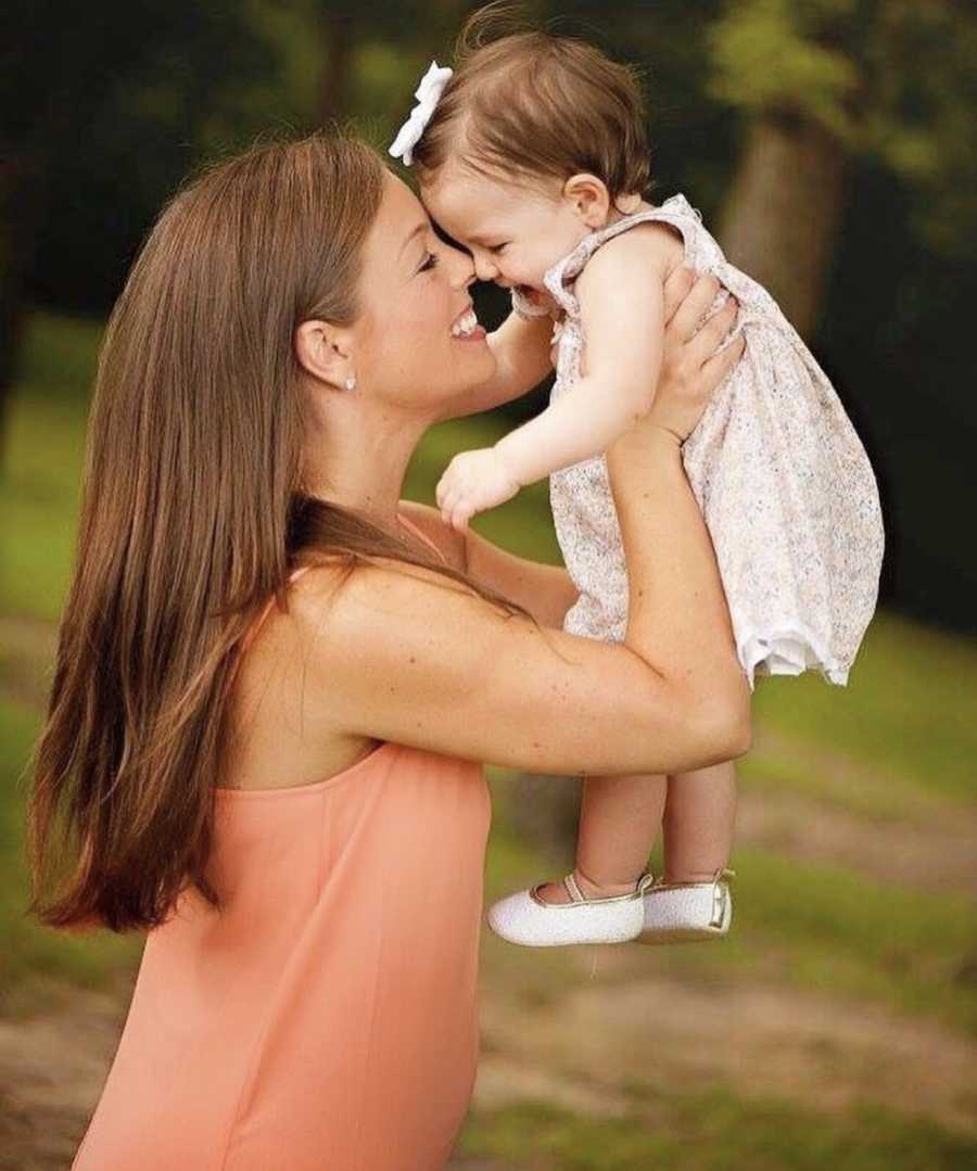 Mother smiles as she holds her autistic baby daughter in the air