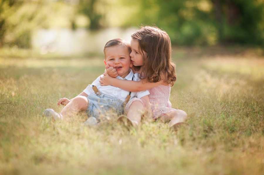 Little girl with autism sits on ground outside hugging baby brother