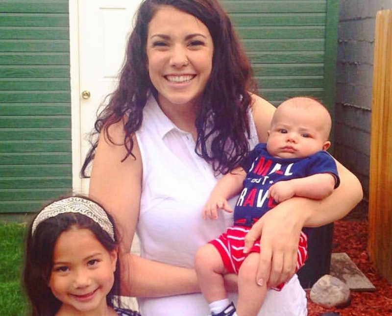 Woman who was in abusive relationship smiles as she holds baby son with daughter standing beside her