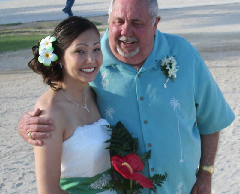 Bride smiles on beach as her father stands with his arm around her