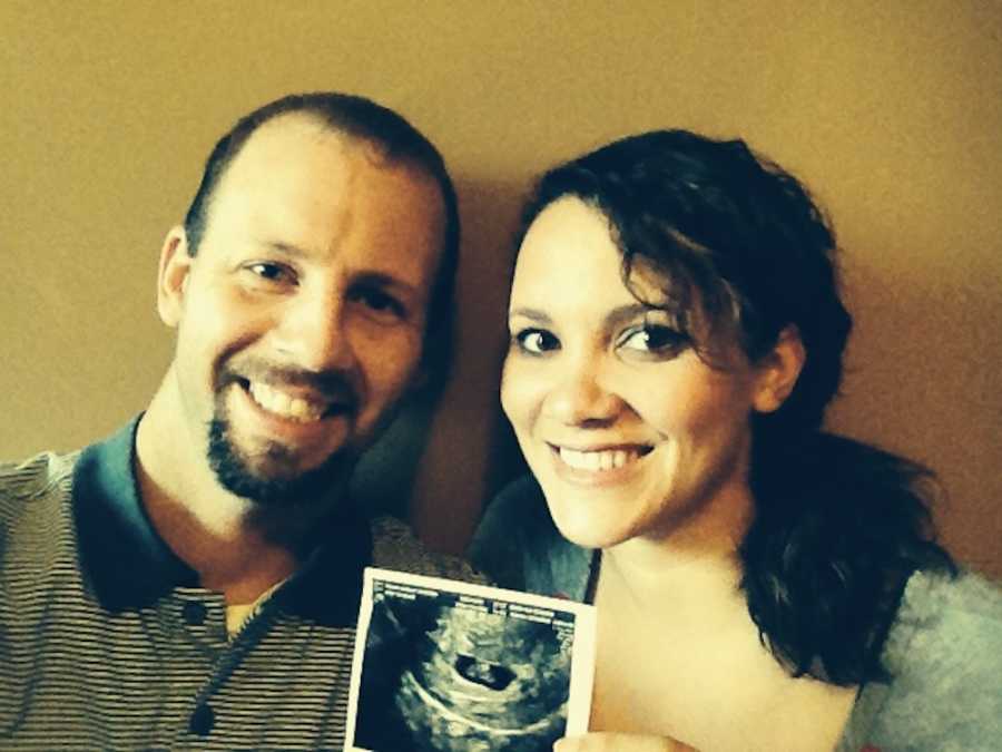 Husband and wife who struggled with fertility smile as wife holds picture of ultrasound