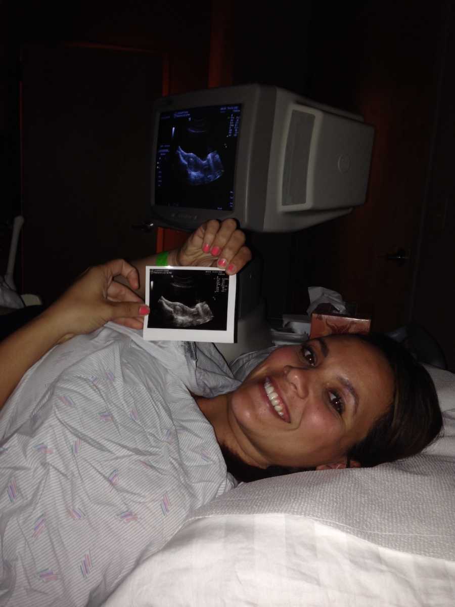 Woman who went through IVF injections lays in doctor's office smiling while holding ultrasound picture