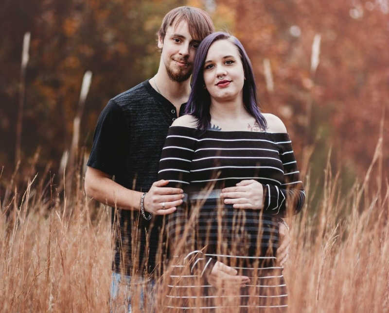 Pregnant woman stands in field with husband whose baby won't fully develop