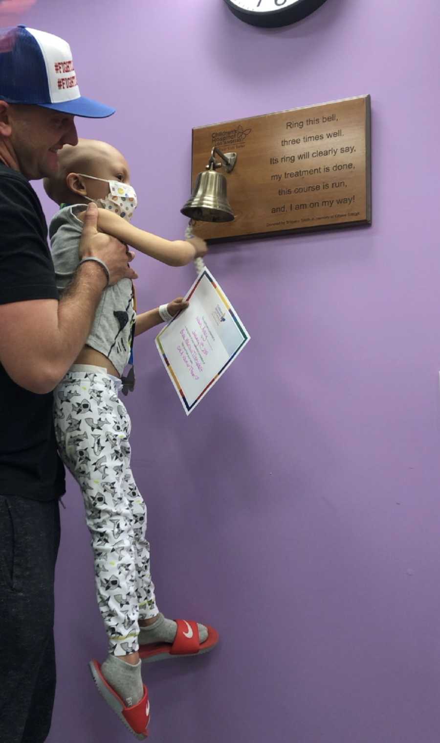 Father holds up son who beat brain cancer to ring bell that signifies end of treatment