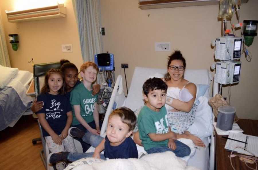 Woman smiles in hospital bed with her newborn beside her five foster children