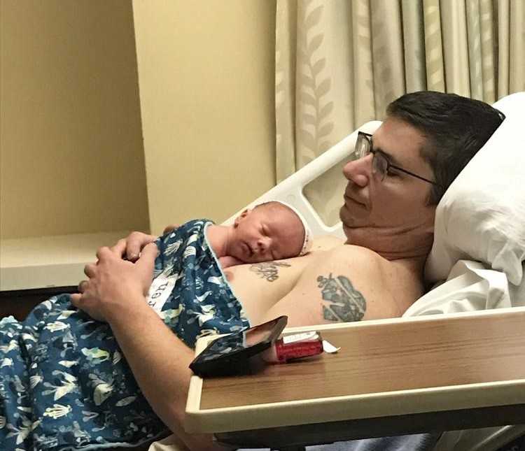 Shirtless father lays in hospital bed with newborn laying on his chest