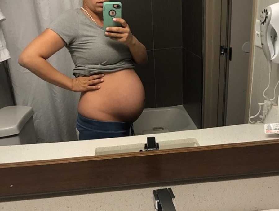 Pregnant woman stands with exposed stomach in mirror selfie
