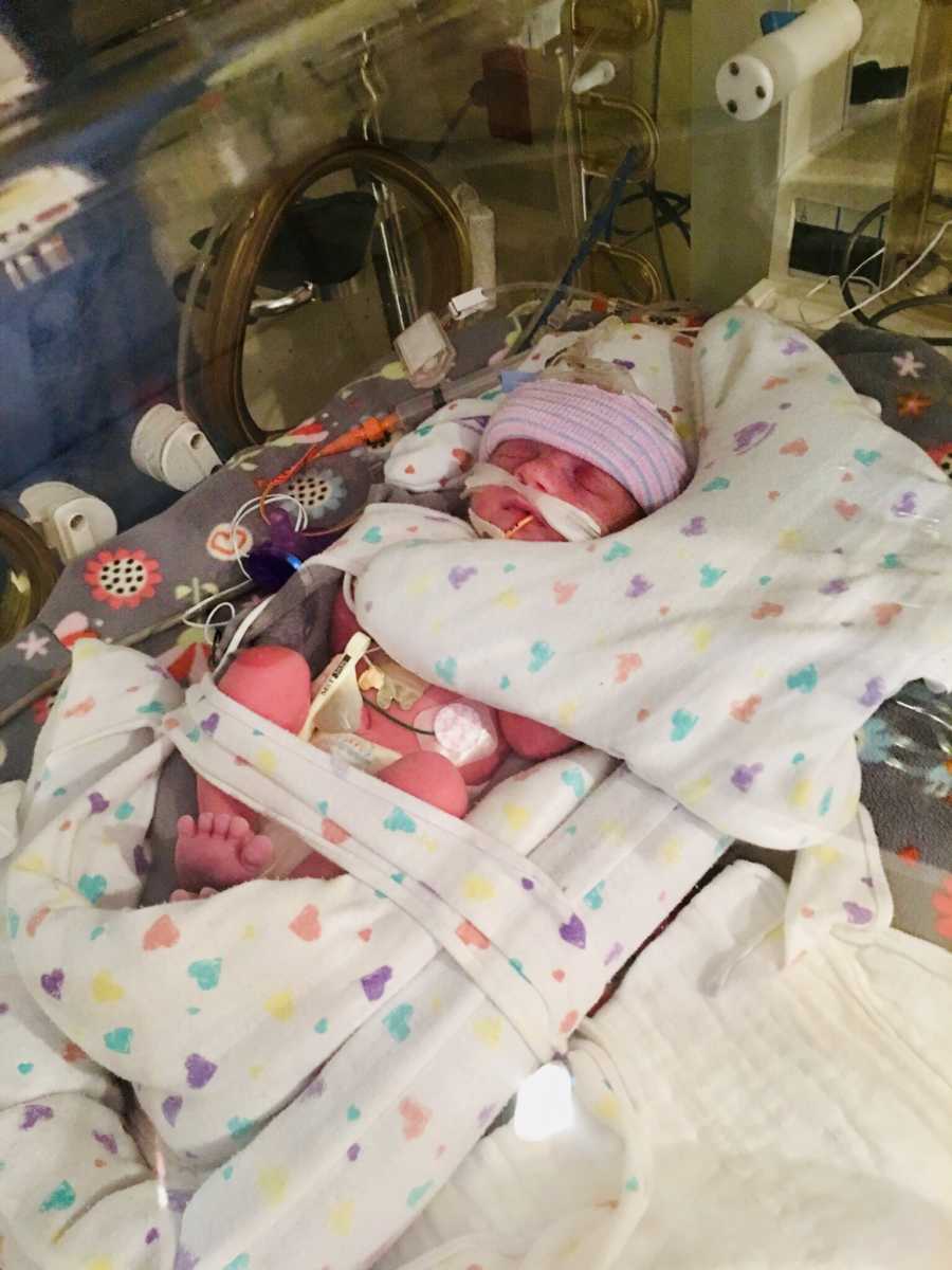 Newborn girl lays in NICU on blanket with colorful hearts all over it