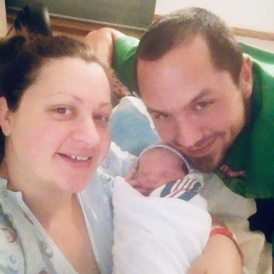 Mother smiles in selfie as she holds newborn in her arm beside late husband