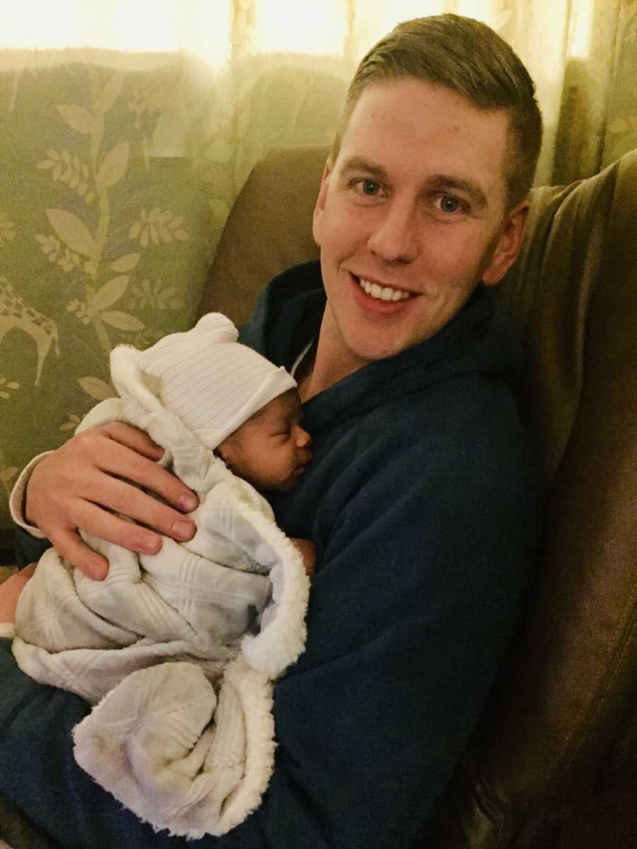 Father sits smiling as he holds adopted newborn to his chest