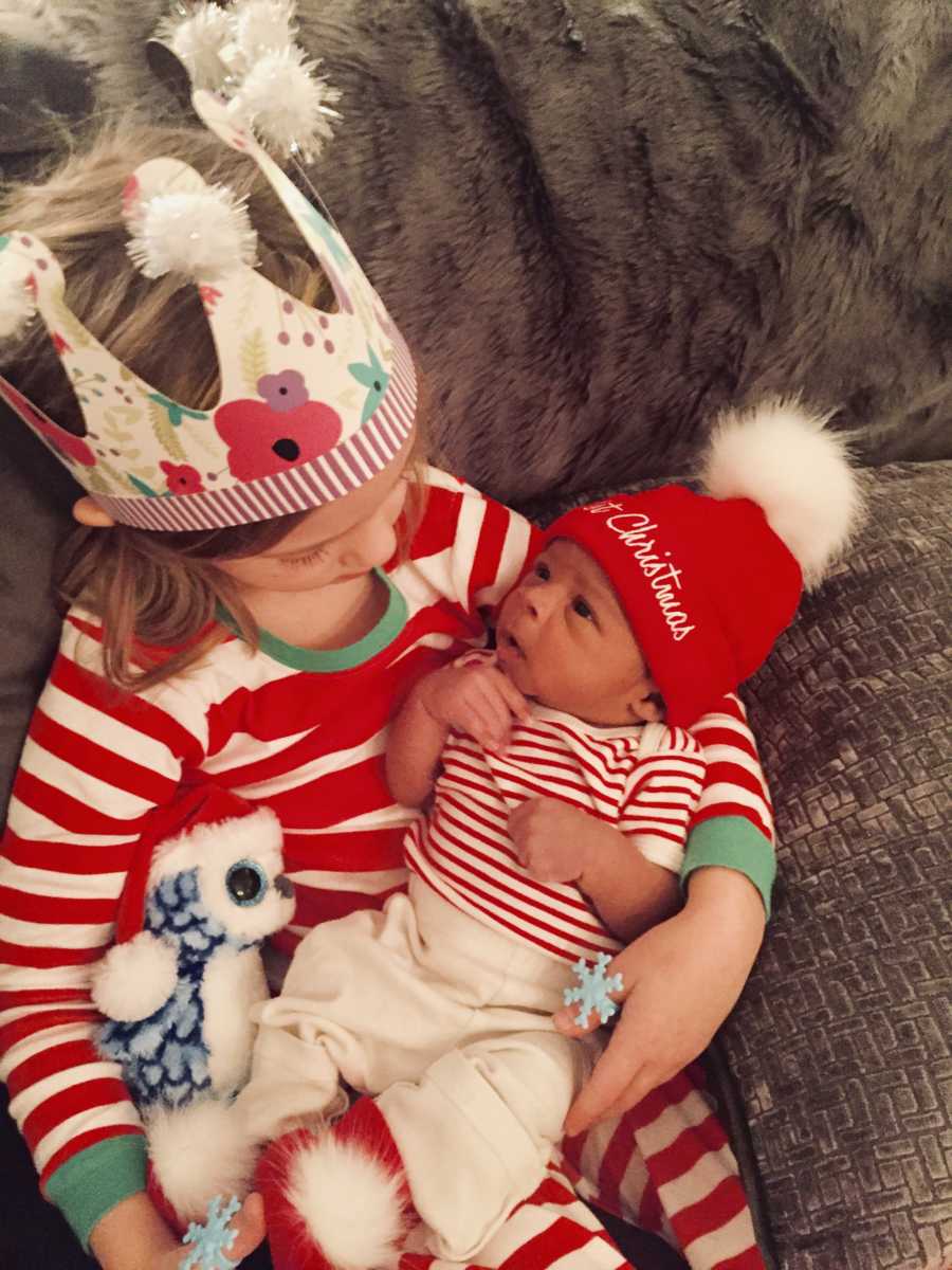 Little girl sits on couch looking at adopted baby brother in her lap