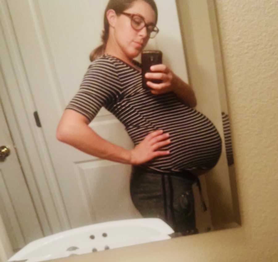 Pregnant woman stands with hand on hip in mirror selfie