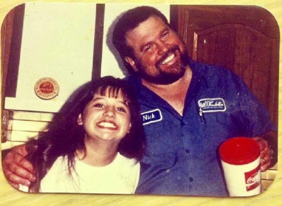 Father stands in home smiling with arm around daughter