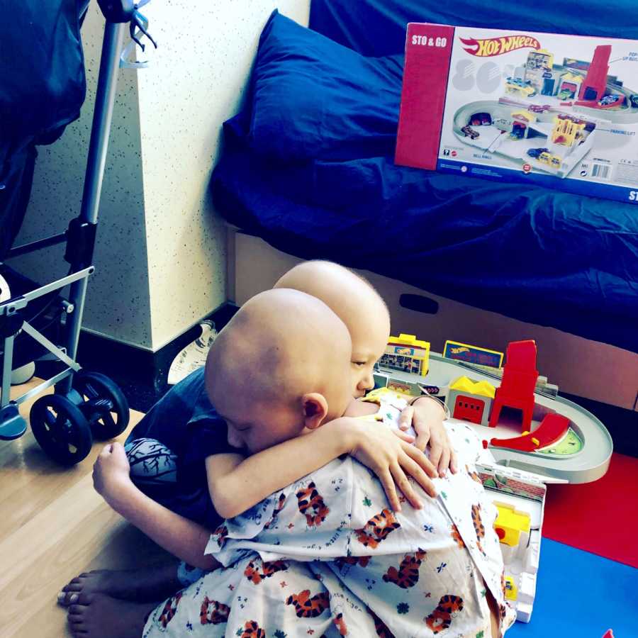 Siblings with brain cancer sit on floor of hospital room hugging