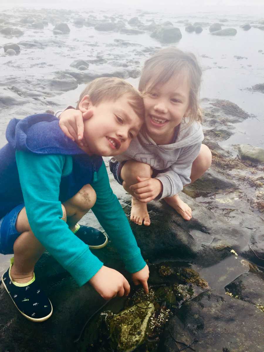 Young siblings who beat brain cancer crouch on rock near body of water 