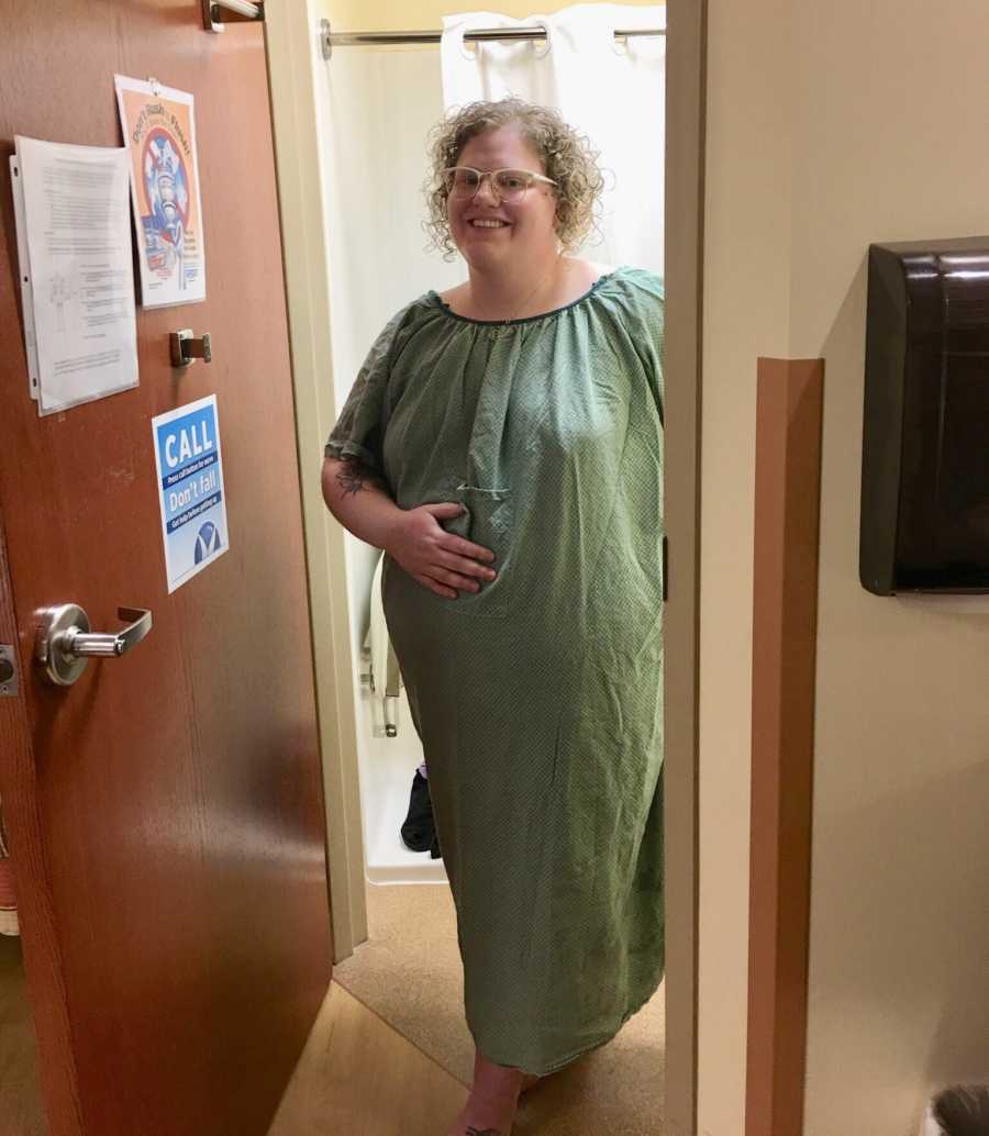 Pregnant woman stands smiling in hospital room bathroom