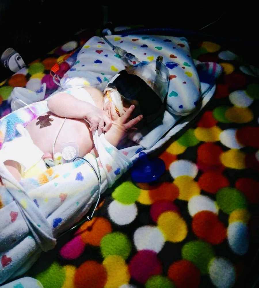 Newborn lays on back in NICU under light with eye covers on