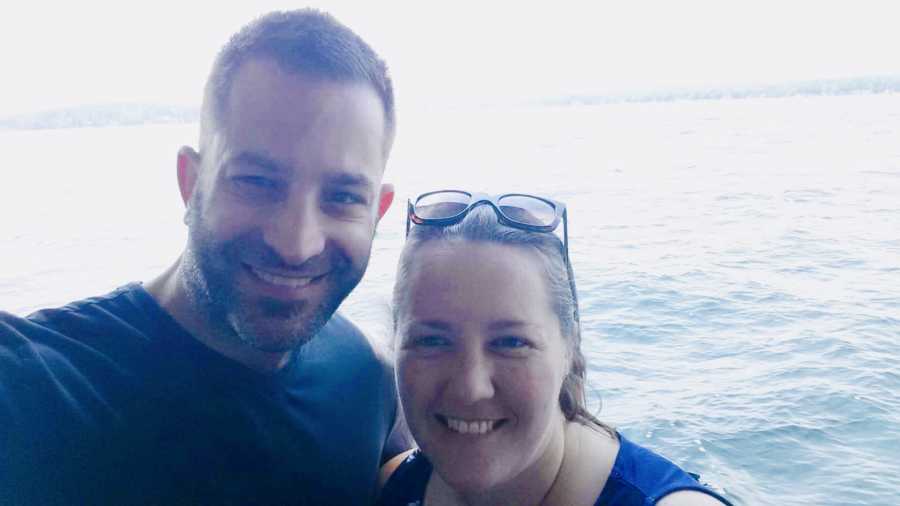 Husband and wife smile in selfie with body of water in background