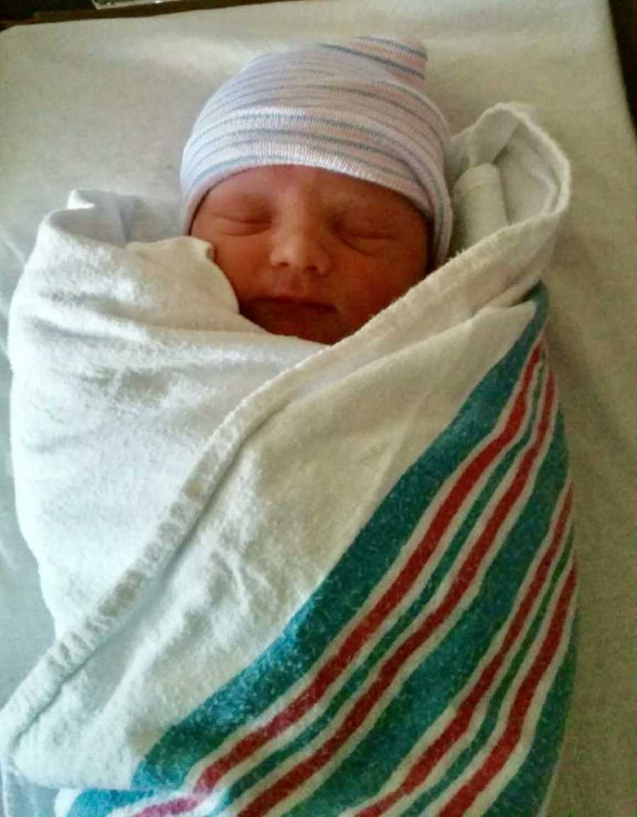 Newborn baby boy lays asleep swaddled in hospital blanket