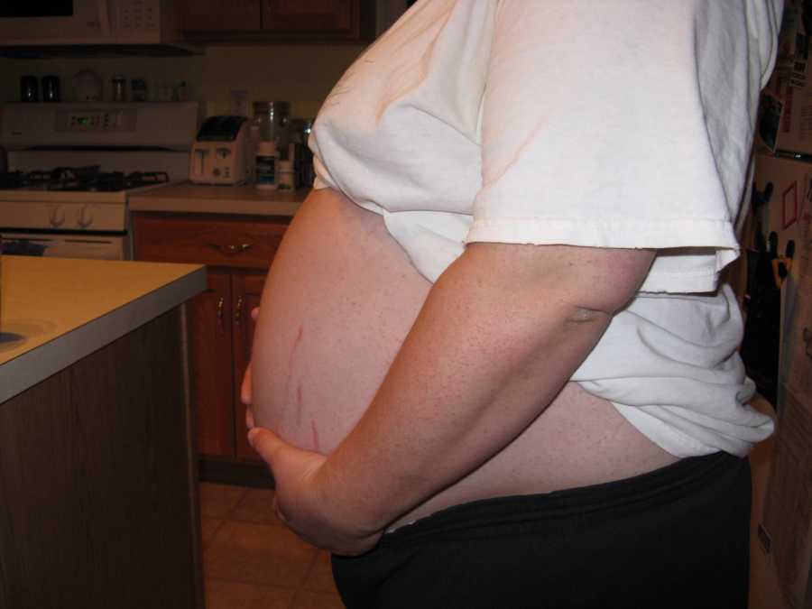 Pregnant woman stands in kitchen holding stomach