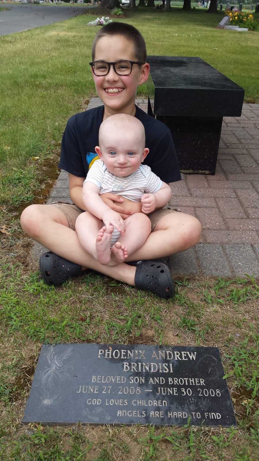 Young boy sits by twin's grave who died at birth, with baby brother sitting in his lap