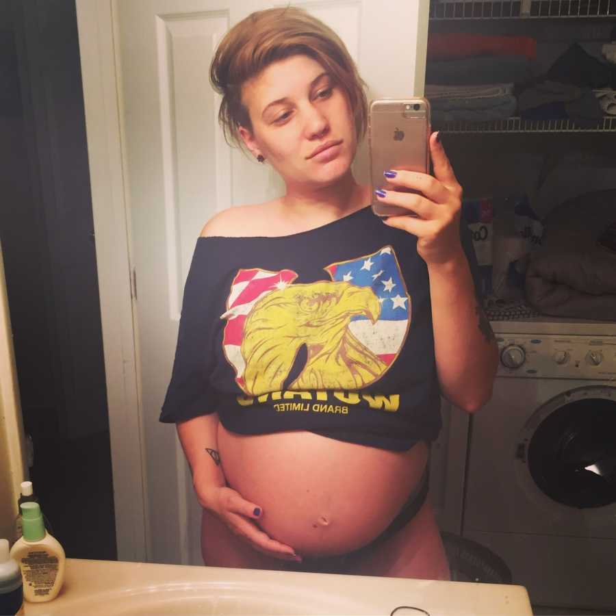 Pregnant woman stands in bathroom taking mirror selfie with stomach exposed