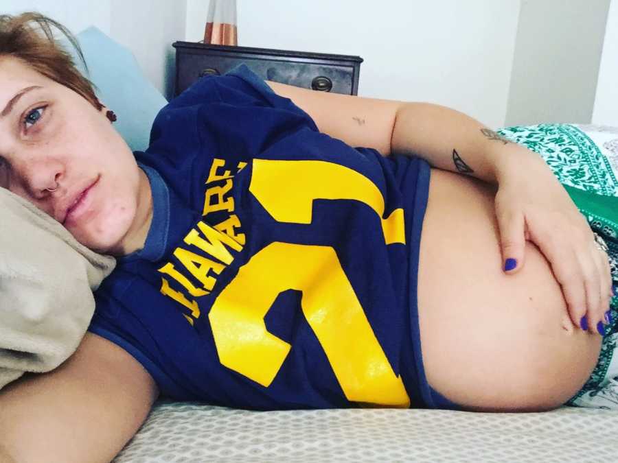 Pregnant woman lays in bed on her side holding her exposed stomach