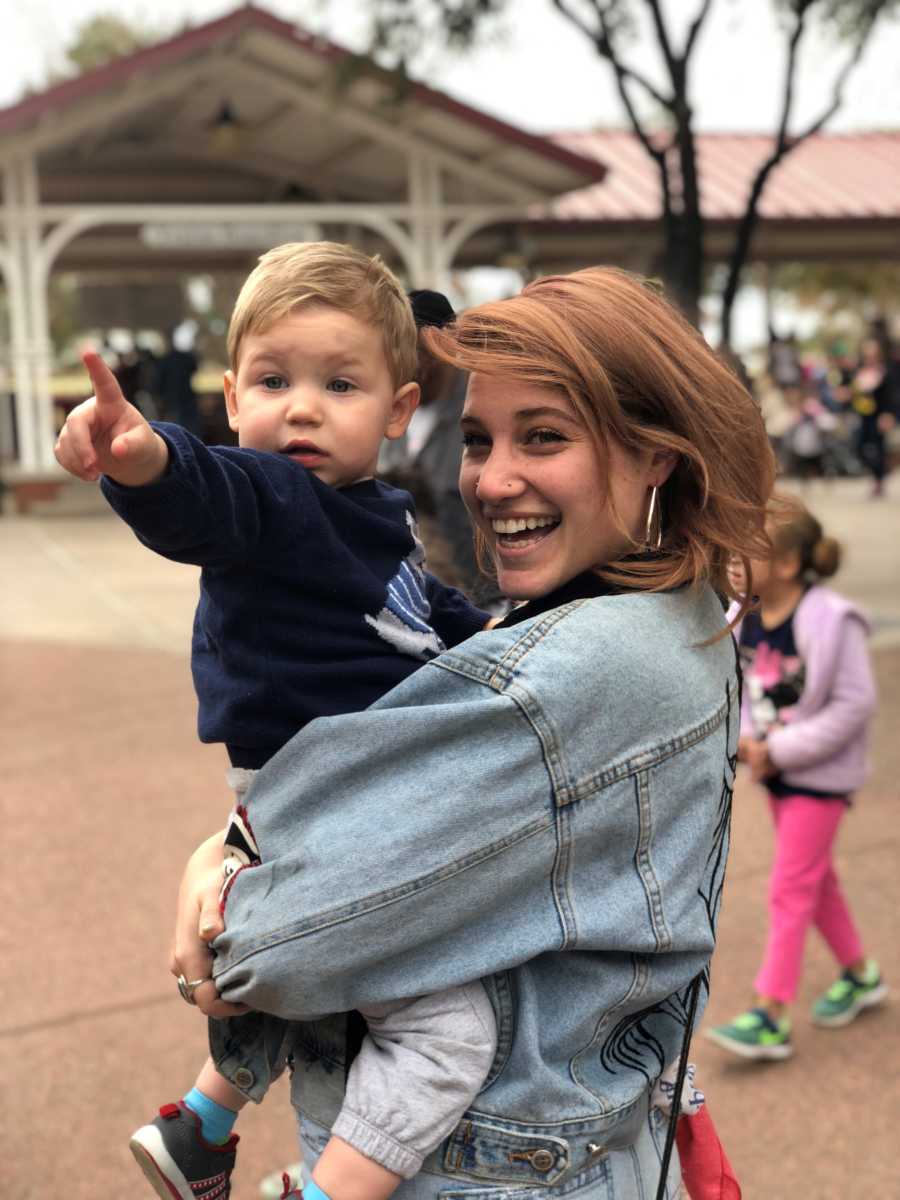 Single mother smiles as she stands outside holding her son that points to something