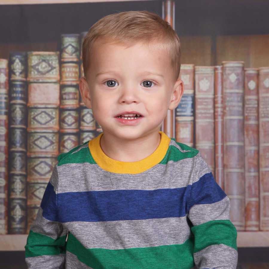 Little boy in foster care smiles for school picture with backdrop of books on shelf